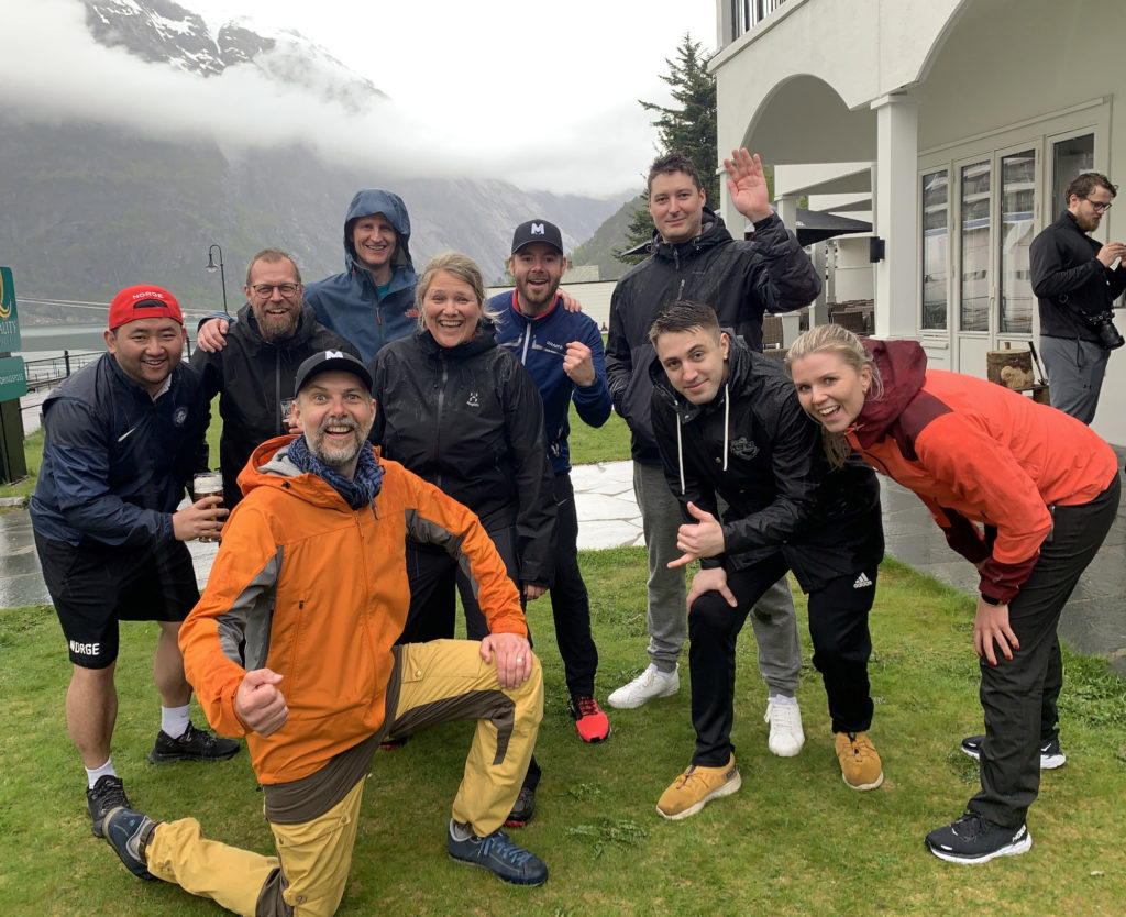 Ant with his colleagues at Maksimer, posing in victory in the rain in Eidfjord, on grass, outside a hotel. Cloud wraithed mountains behind.