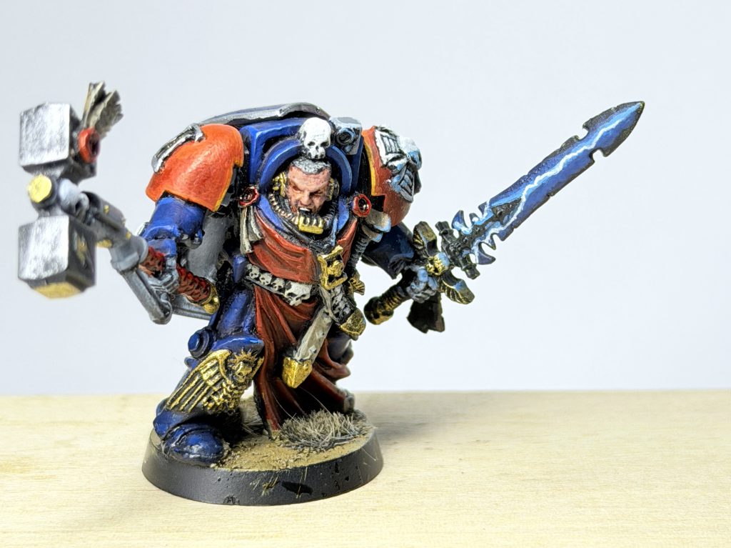 Lord Inquisitor Arcturus wields a thinder hammer and daemon sword and wears deep blu terminator armour with red robes